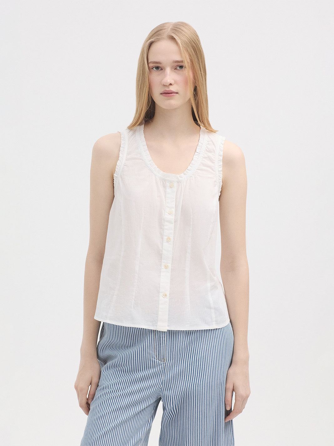 Woman wearing a white sleeveless blouse and blue striped pants on a light gray background